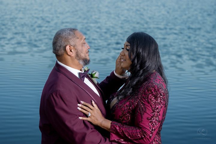 Romantic couple in burgundy and wine colored formal wear embrace by a serene lake at twilight.