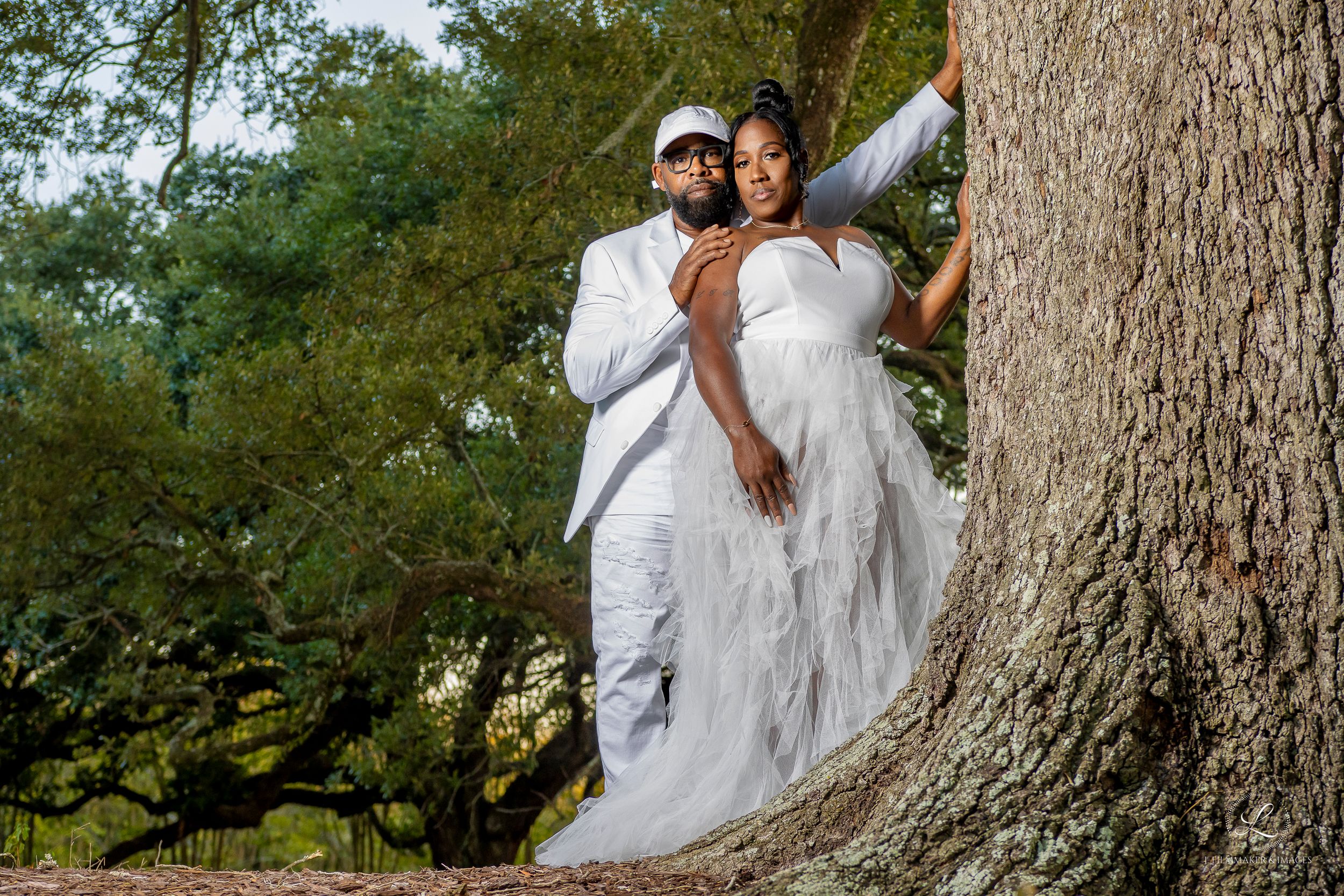 Romantic wedding portraits captured against large tree trunks in a natural setting.