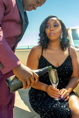 Couple sharing champagne outdoors, with person in burgundy suit pouring into glass.
