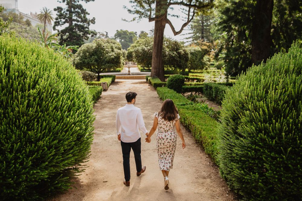 Two people walking along a garden path surrounded by manicured hedges and trees.