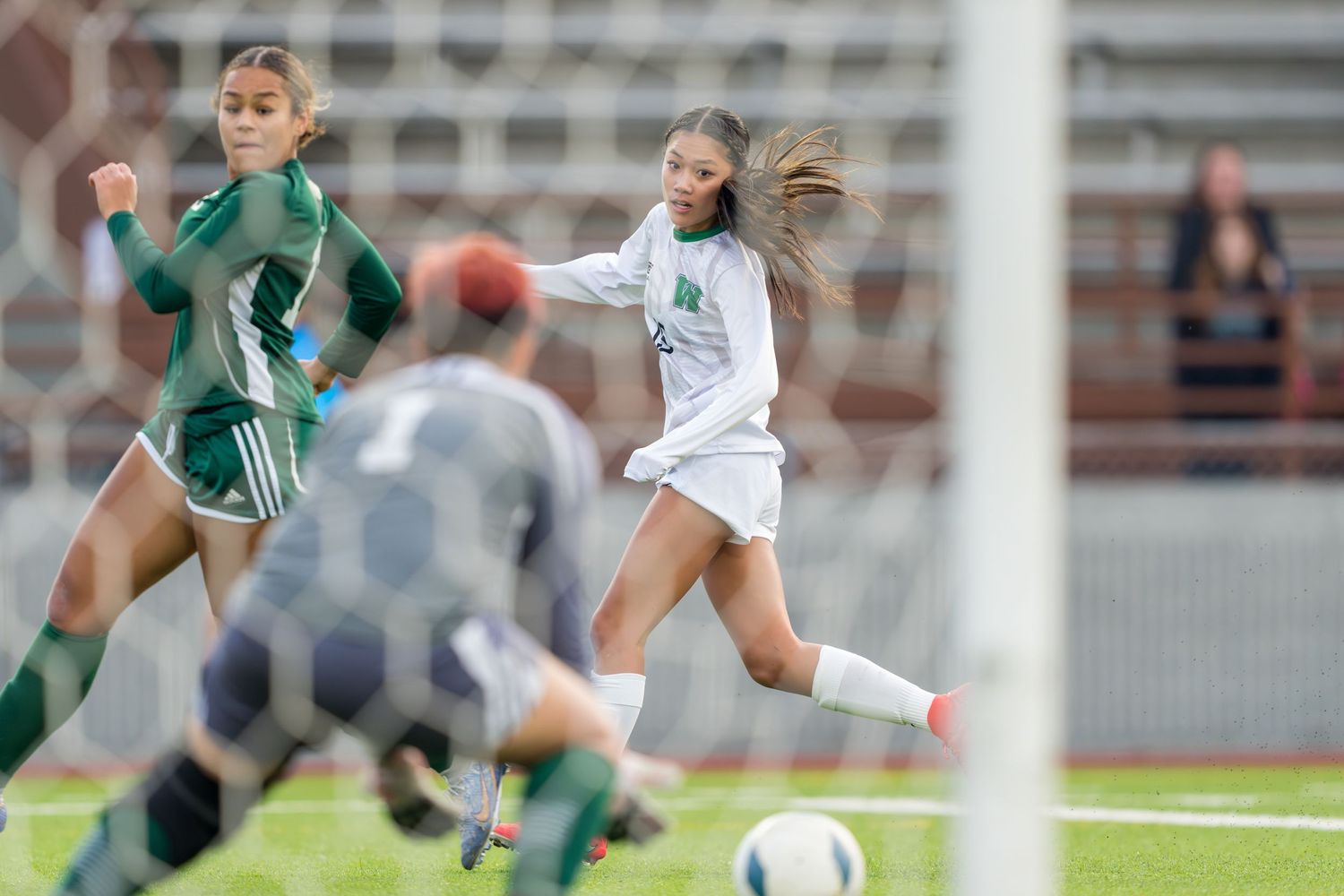 A women's soccer player from Woodinville High School watches her shot attempt at the goal.