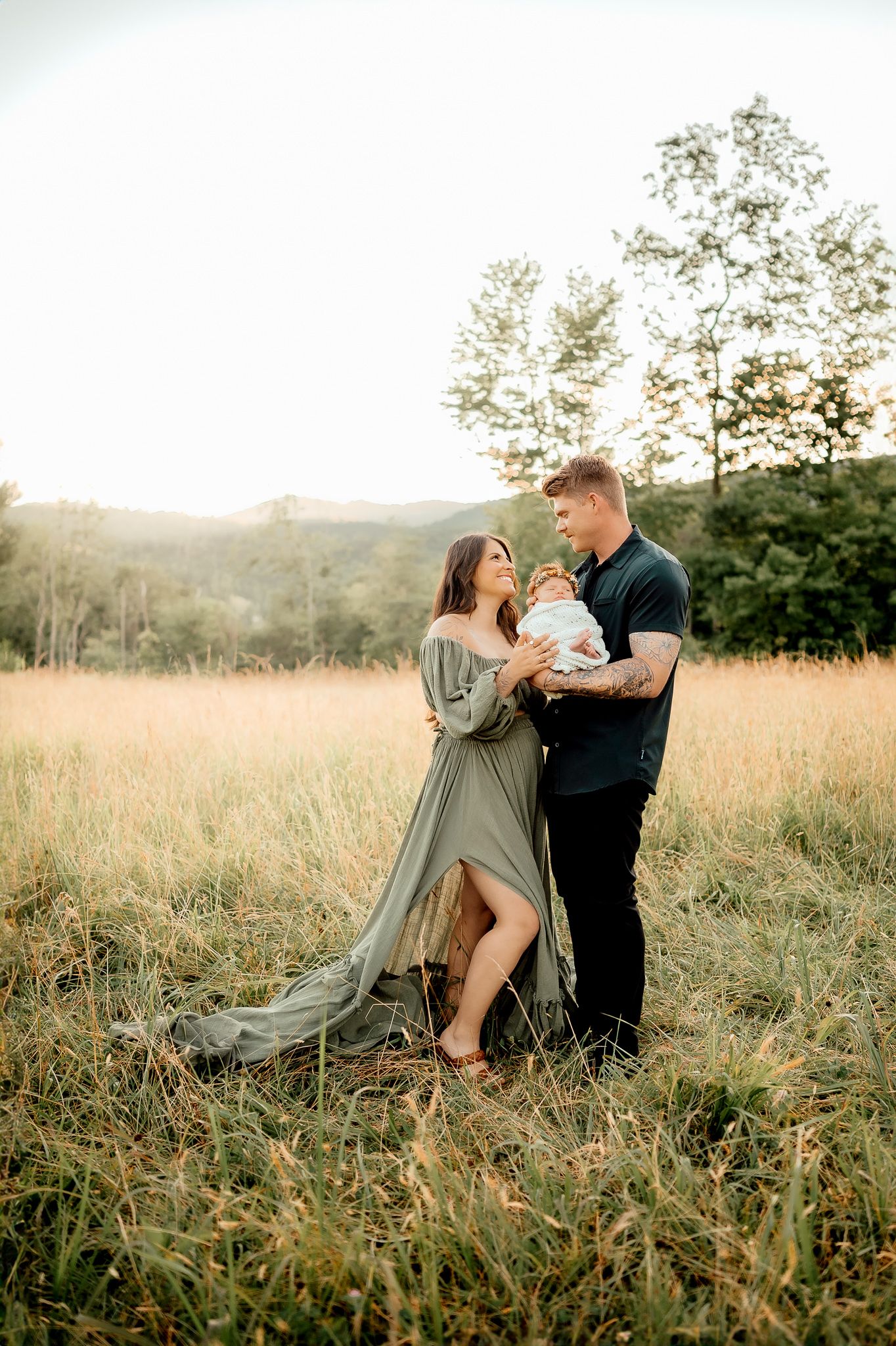 Family of three shares intimate moment in sunlit field.