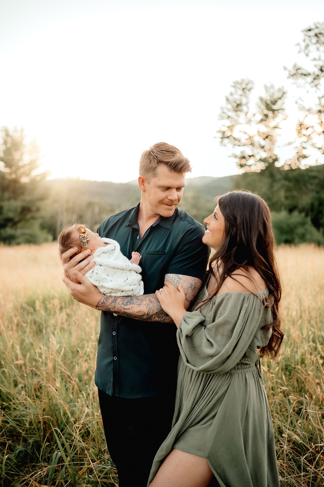 A couple holding their newborn baby in a golden field at sunset.