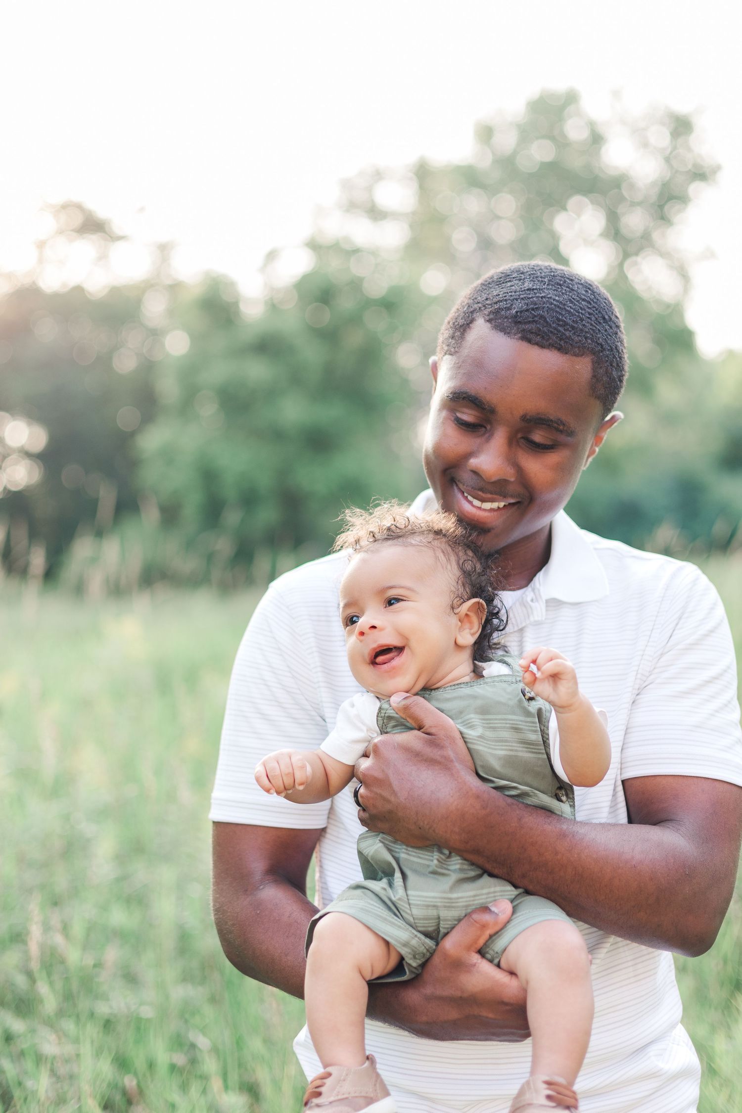 Joyful outdoor portraits showing tender moments between parent and baby in a sunny field.