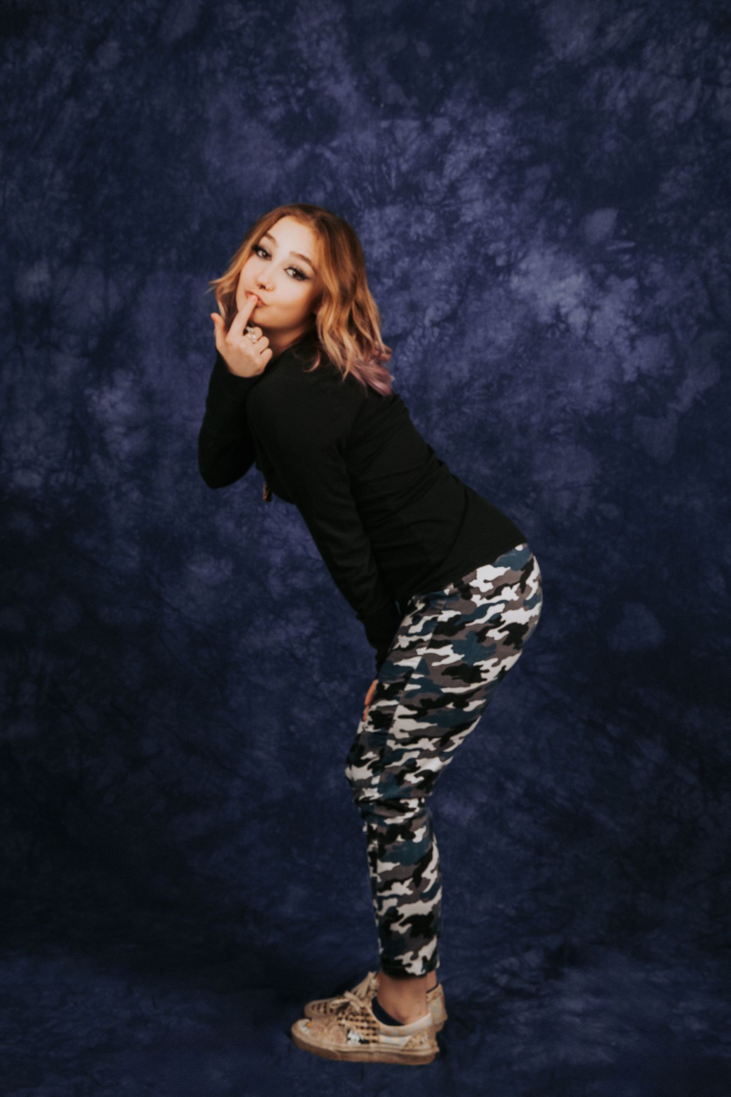 Person in black top and camo pants strikes dynamic poses against dark backdrop.