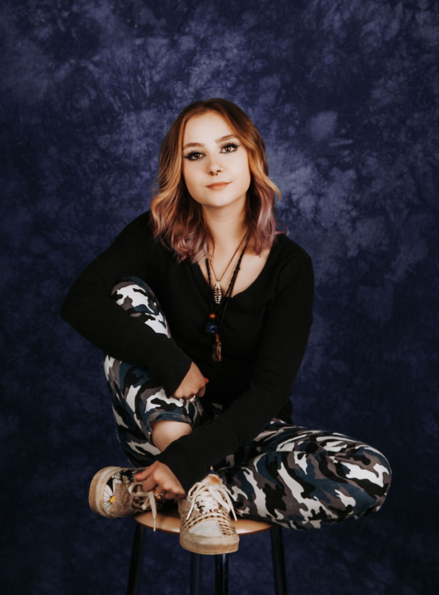 Person in casual black outfit reclines on barstool during studio photoshoot.