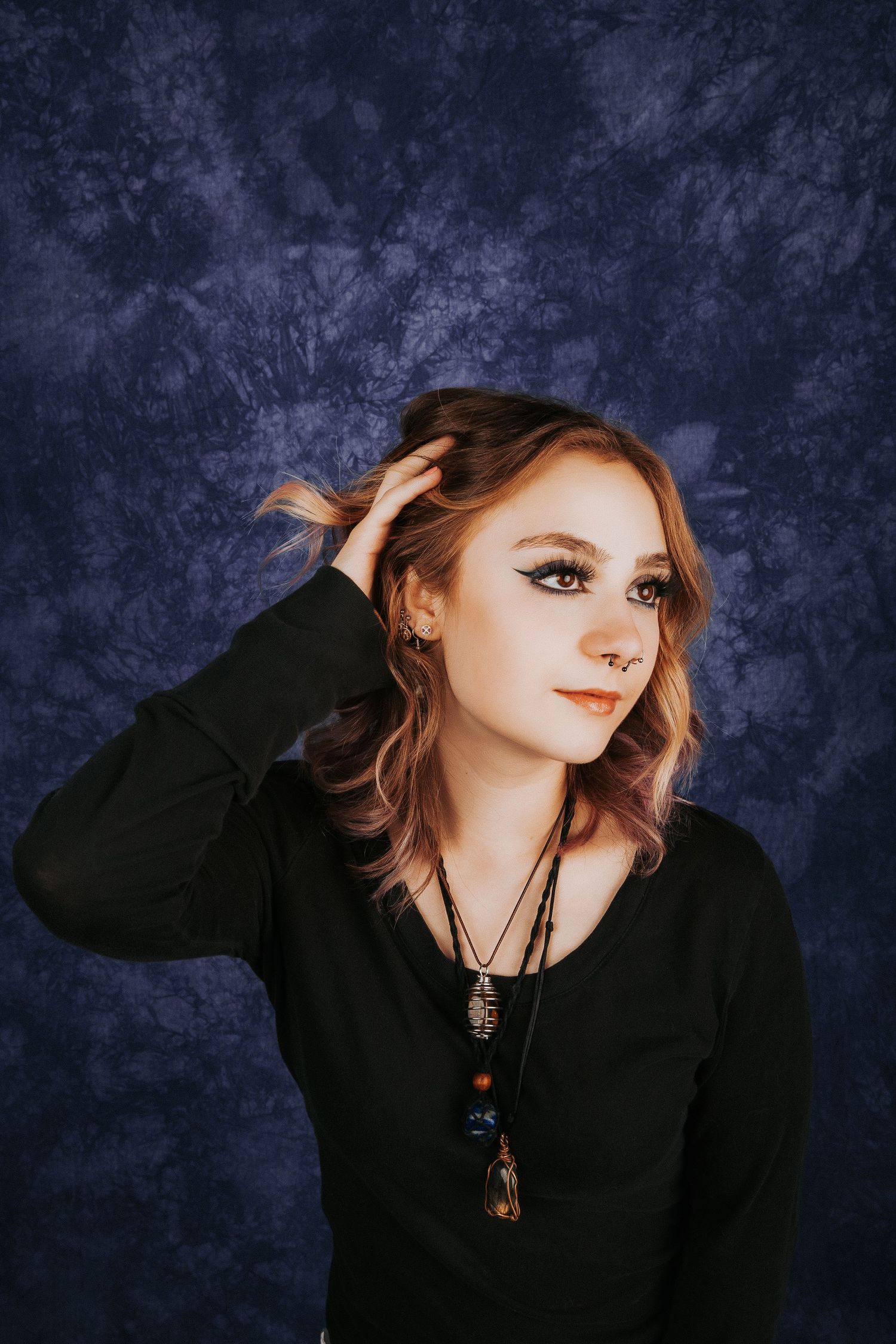 Alternative fashion portrait with dark backdrop showing playful expressions against textured navy background.