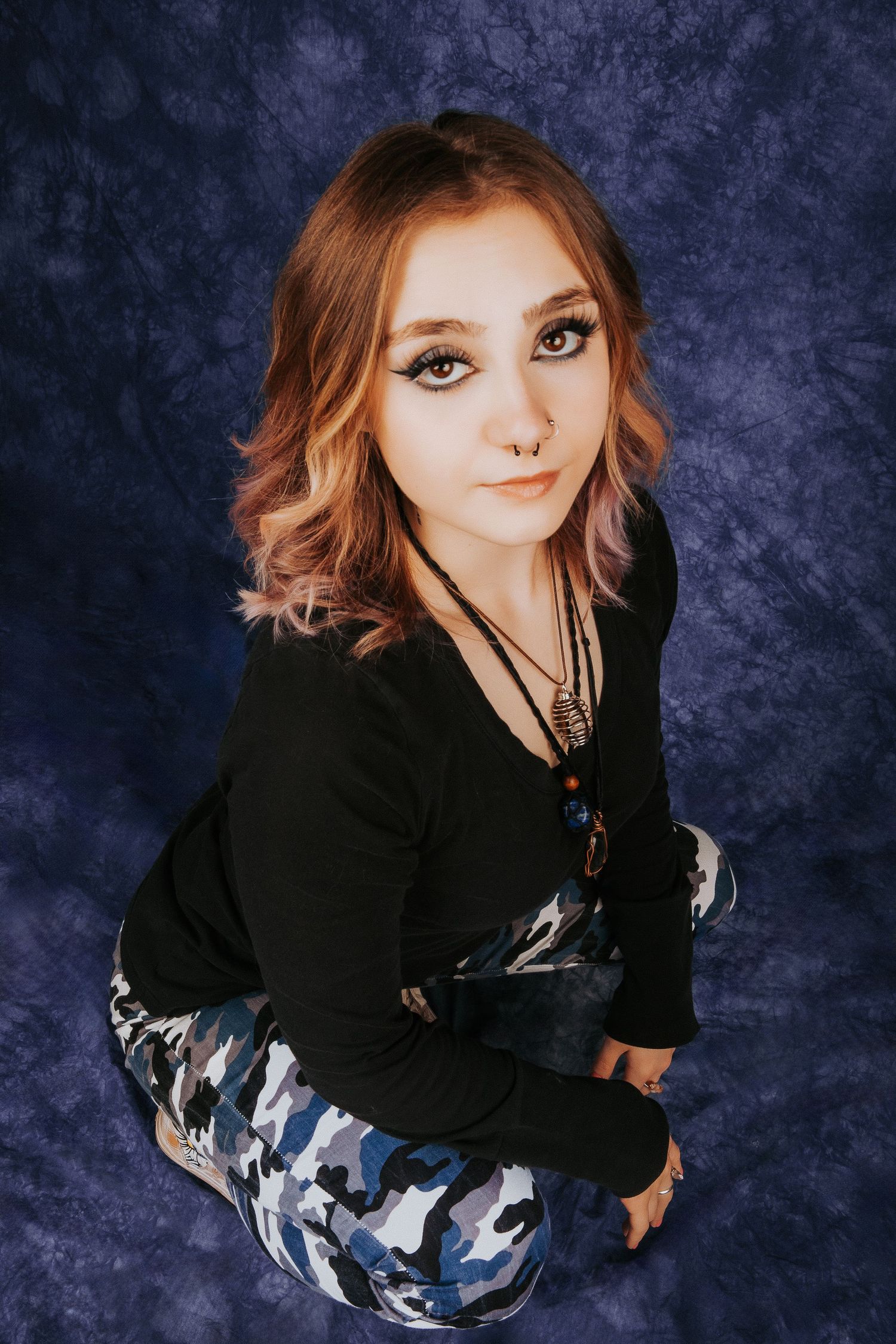 Fashion portrait from above showing edgy style with camo pants against dark blue backdrop.