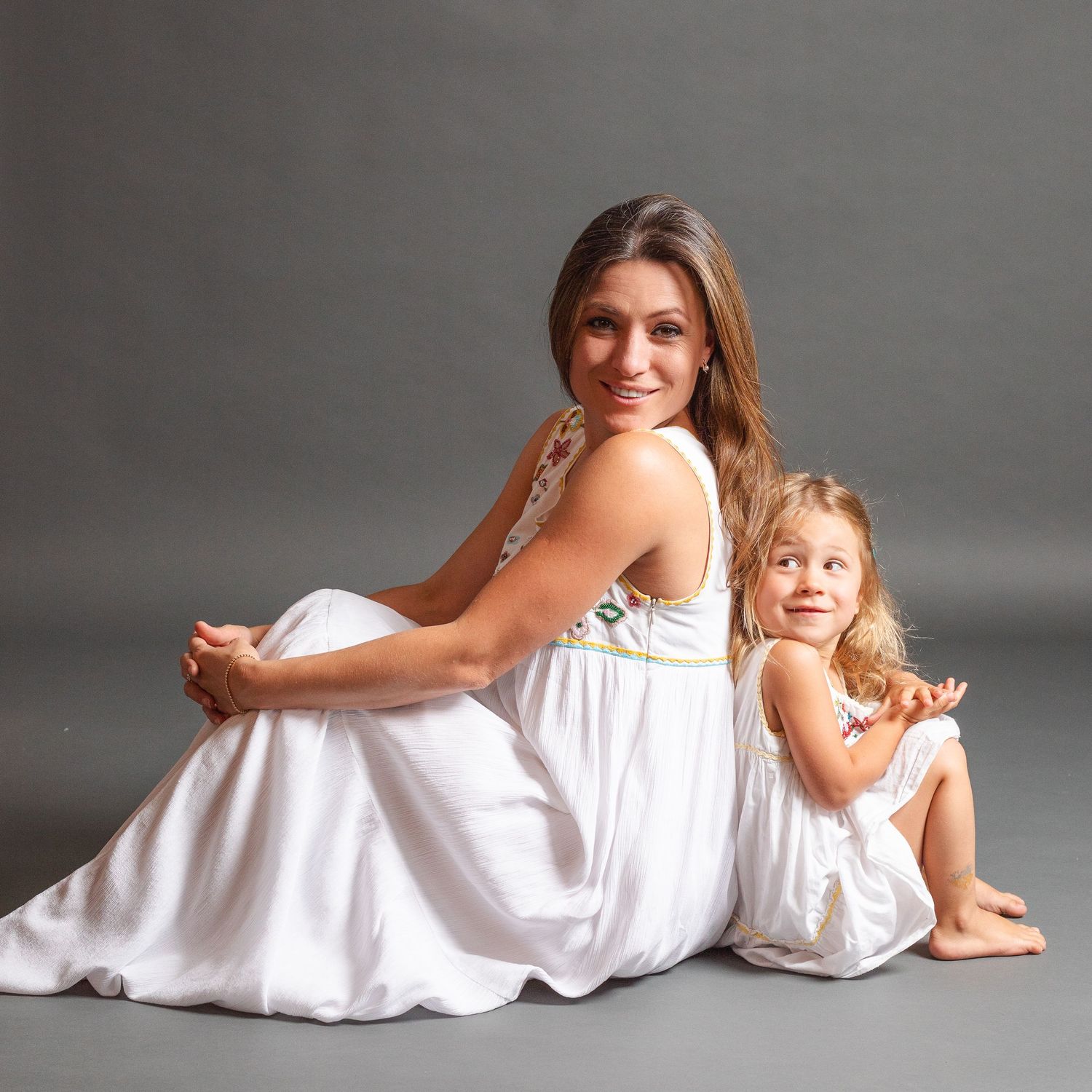 Mother and daughter in white dresses lying down in a minimalist studio setting for a portrait series.