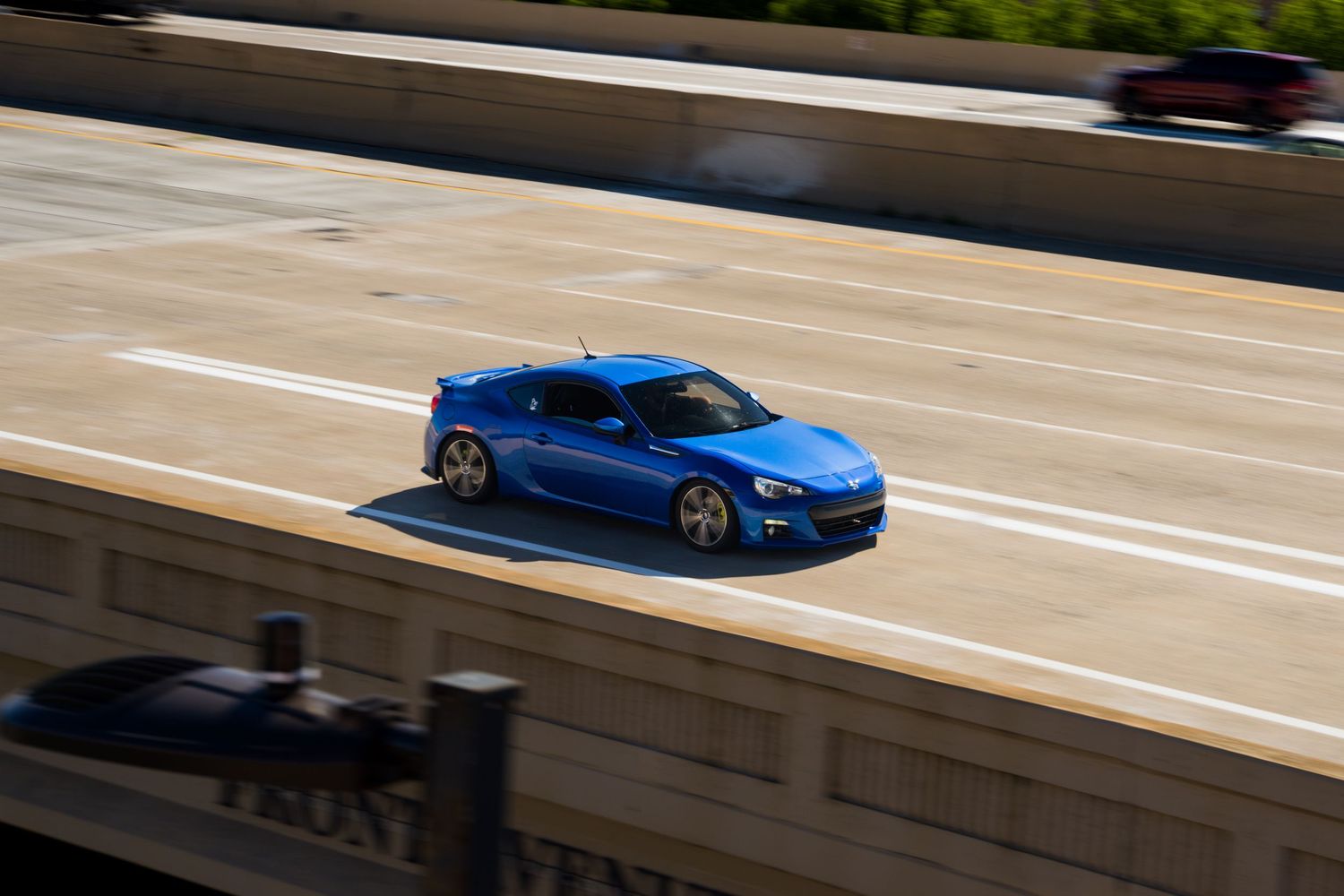 Aerial view of blue sports coupe driving fast on urban highway overpass.