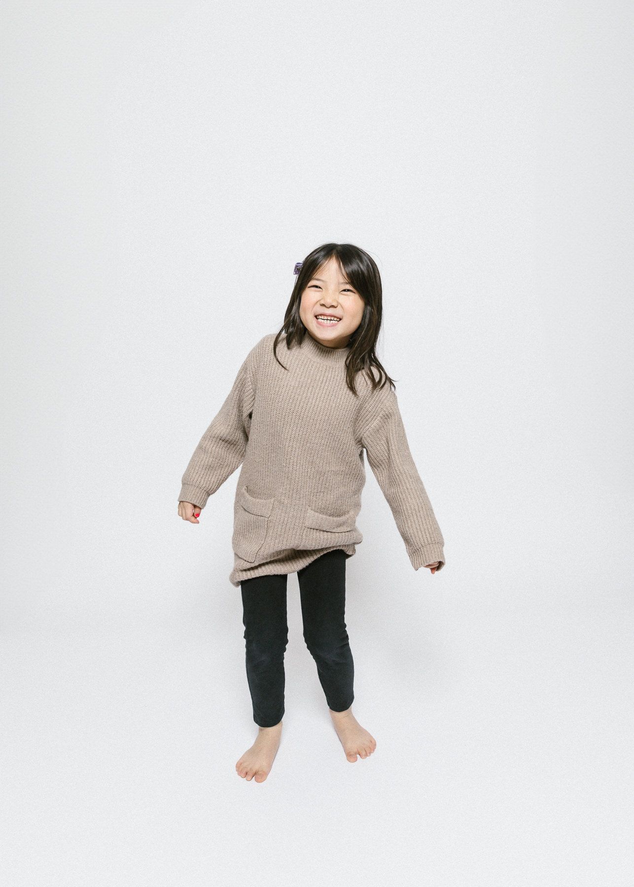 A playful portrait of a child wearing a beige sweater against a white backdrop.