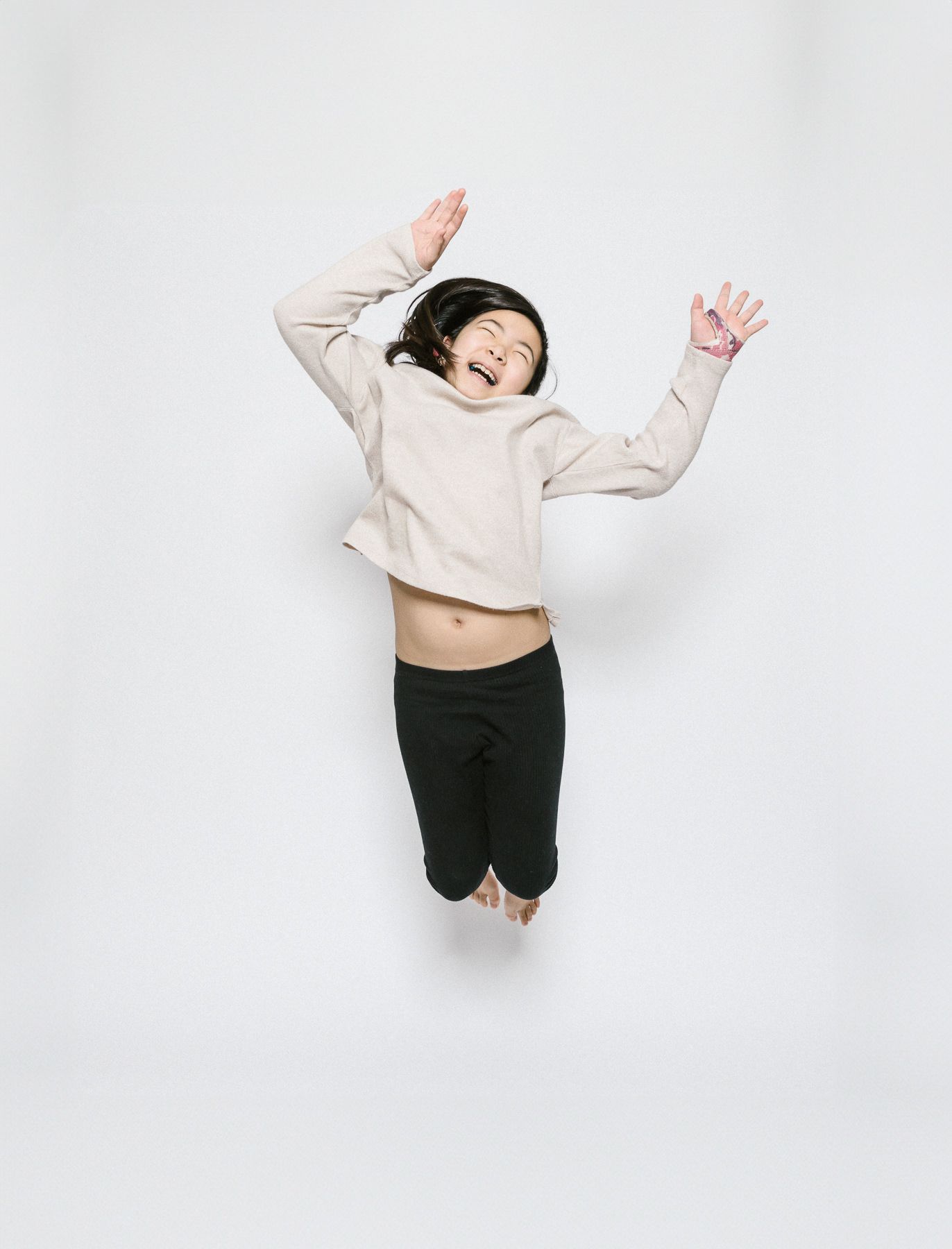 Child in beige sweater jumping joyfully against white background.
