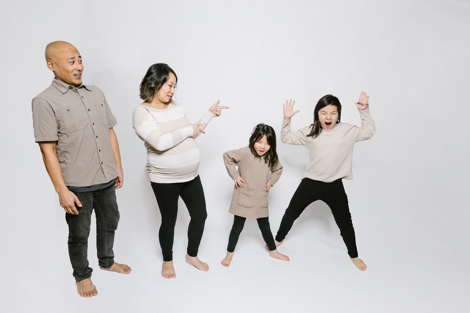 Family in matching neutral tones striking playful poses against white backdrop.