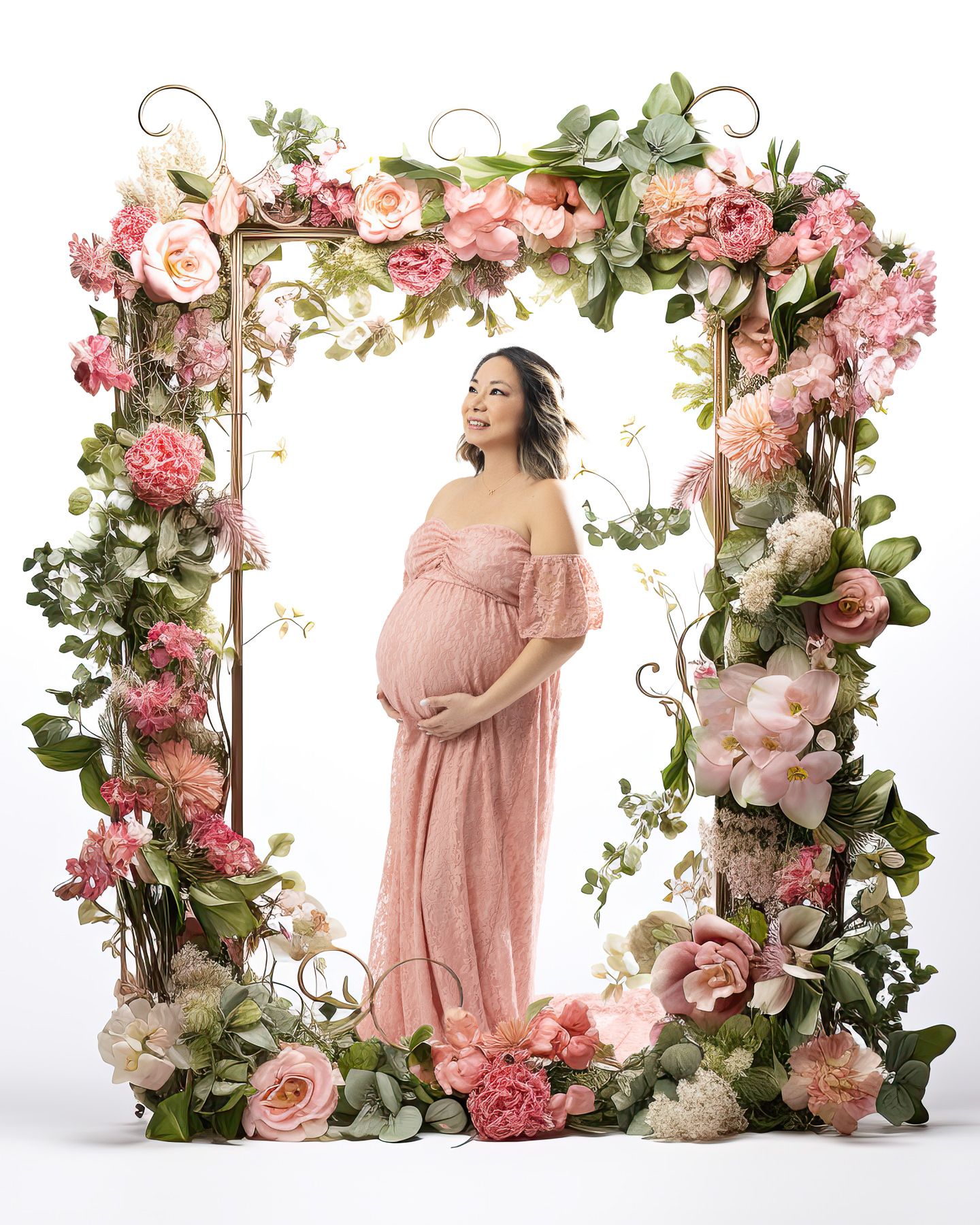 A floral arch with pink roses and greenery frames a maternity scene in soft natural lighting.