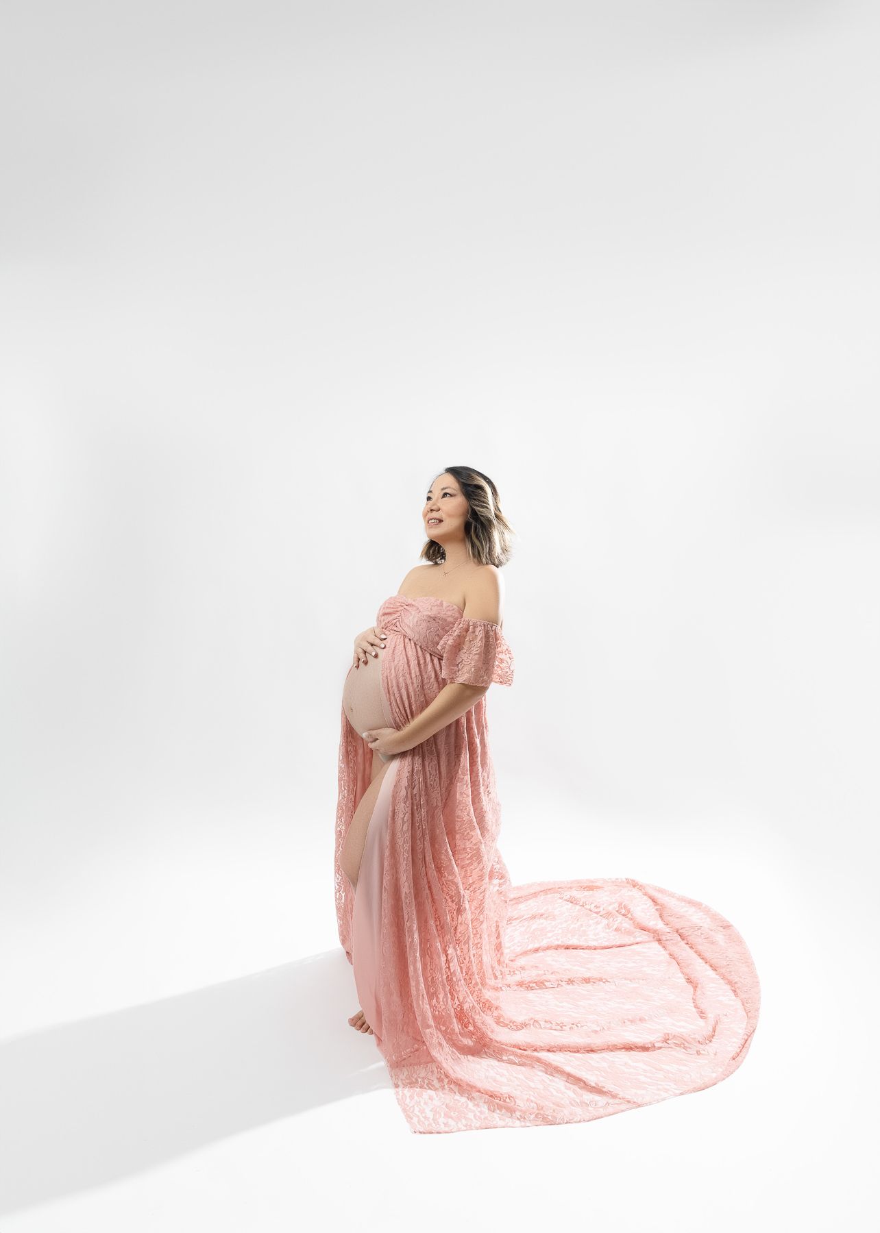Maternity portrait with flowing pink dress against white background.