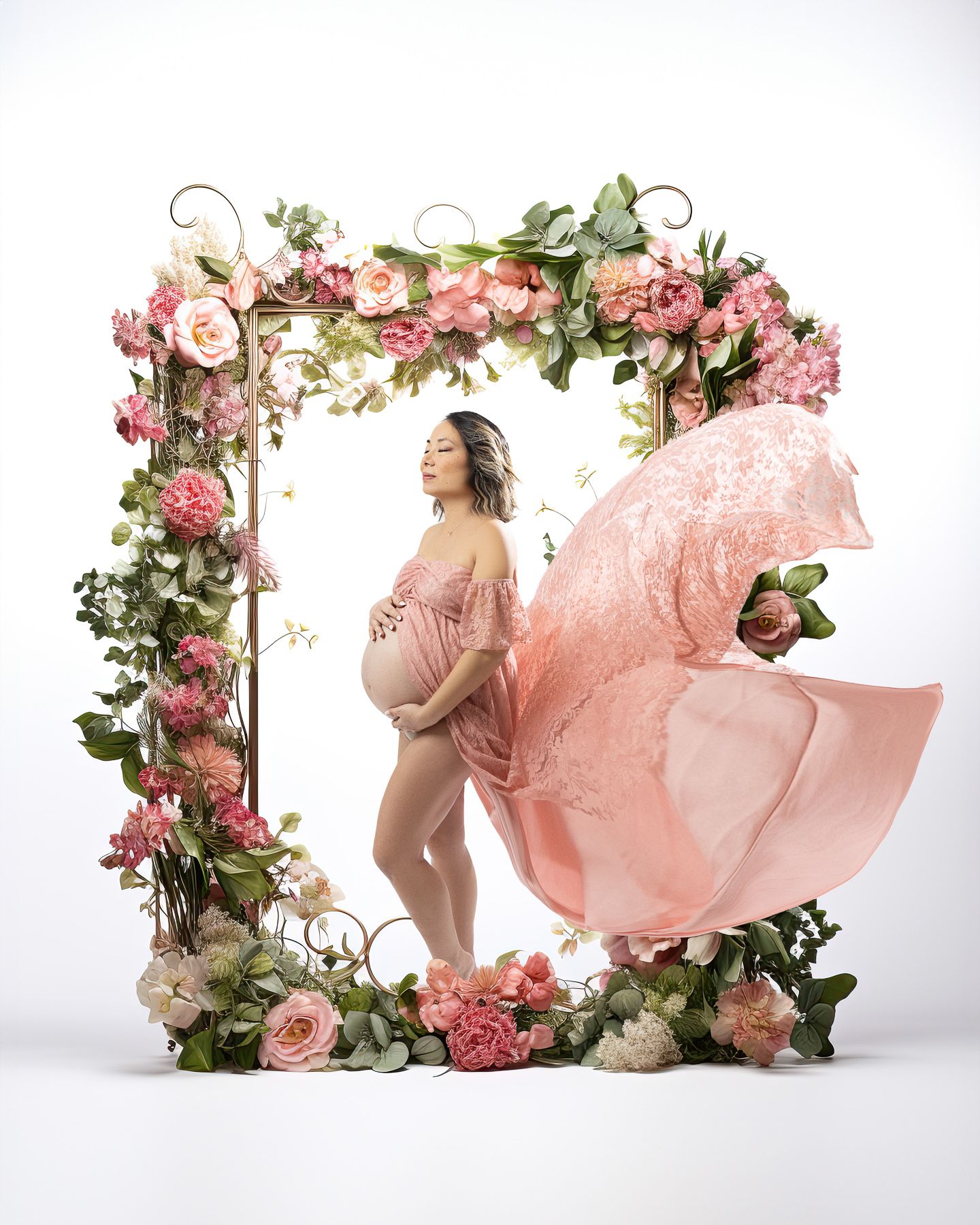 Maternity photo featuring a floral arch with pink roses and flowing fabric.