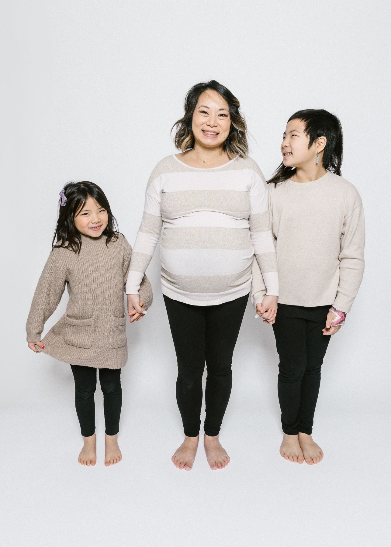 A family wearing coordinating neutral outfits poses together against a white background.