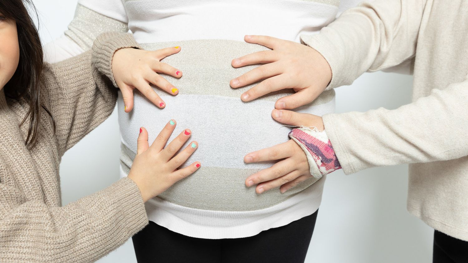 Multiple hands rest lovingly on a pregnant belly in a tender family moment.