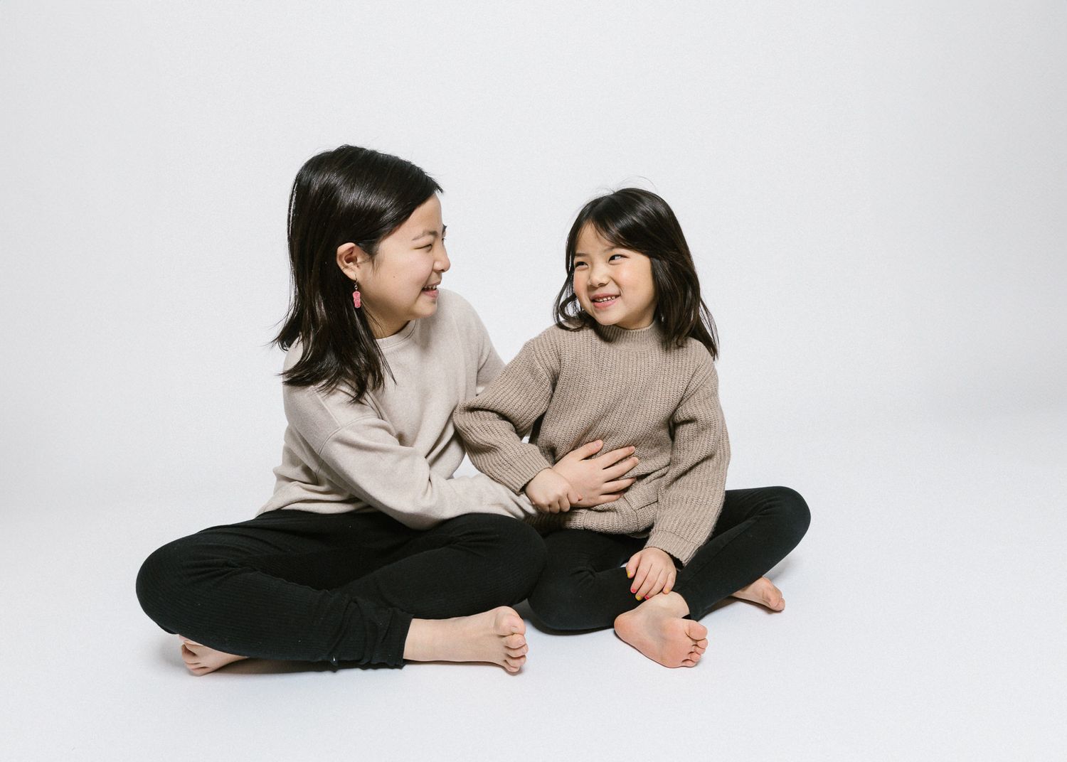 Two young children in matching beige sweaters sitting and laughing together.