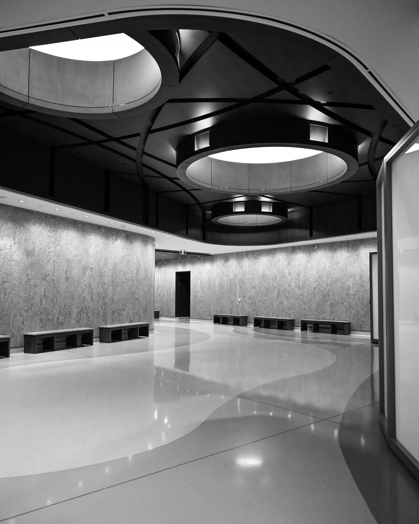Modern interior space with circular skylights and reflective floor creating dramatic lighting effects.