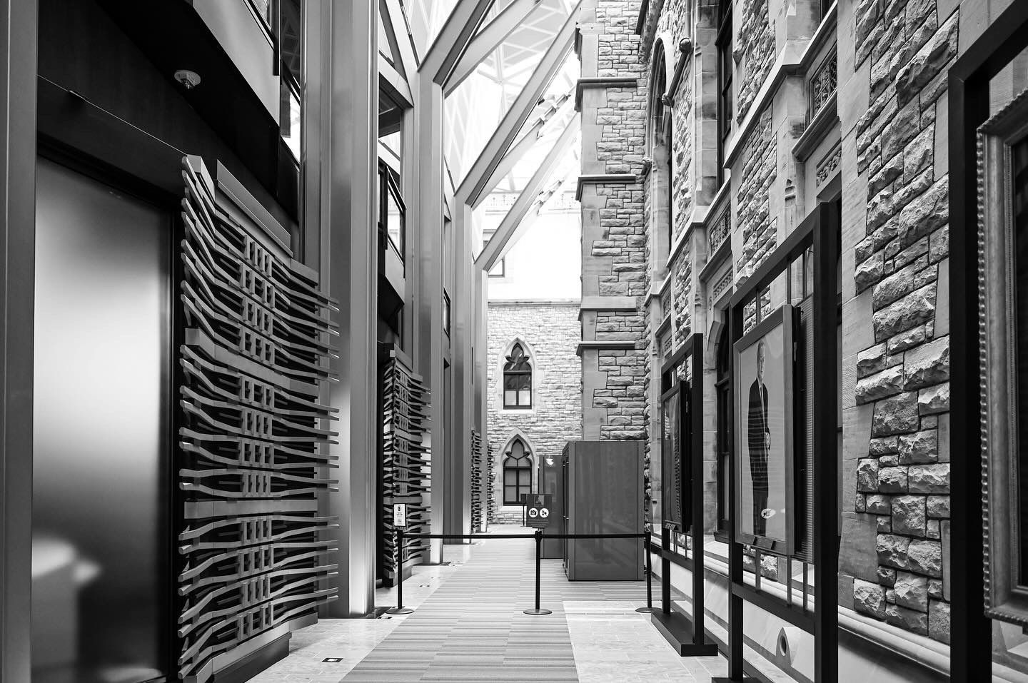 Black and white architectural corridor with stone walls and glass roof leading to church spire.