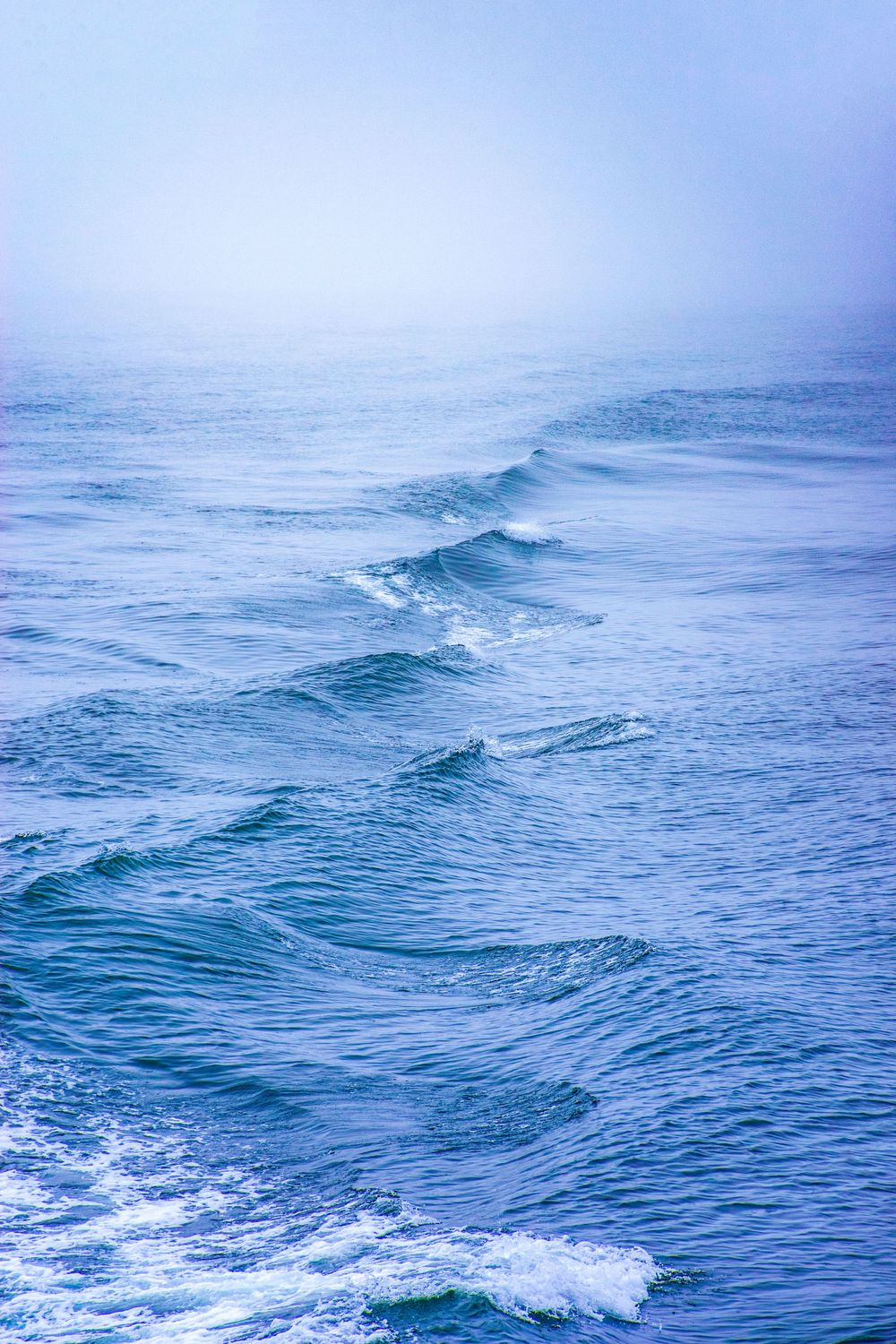 Rolling ocean waves create a serene blue seascape under misty skies.