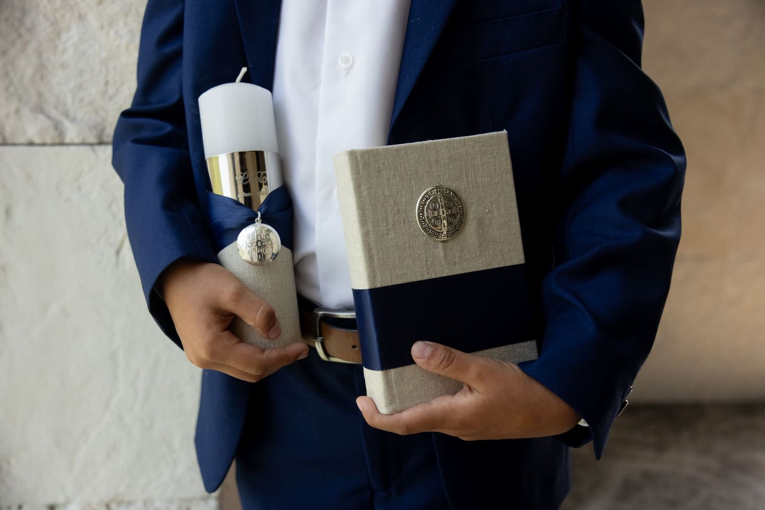 Boy in blue suit holding a white candle and religious book for First Communion ceremony.
