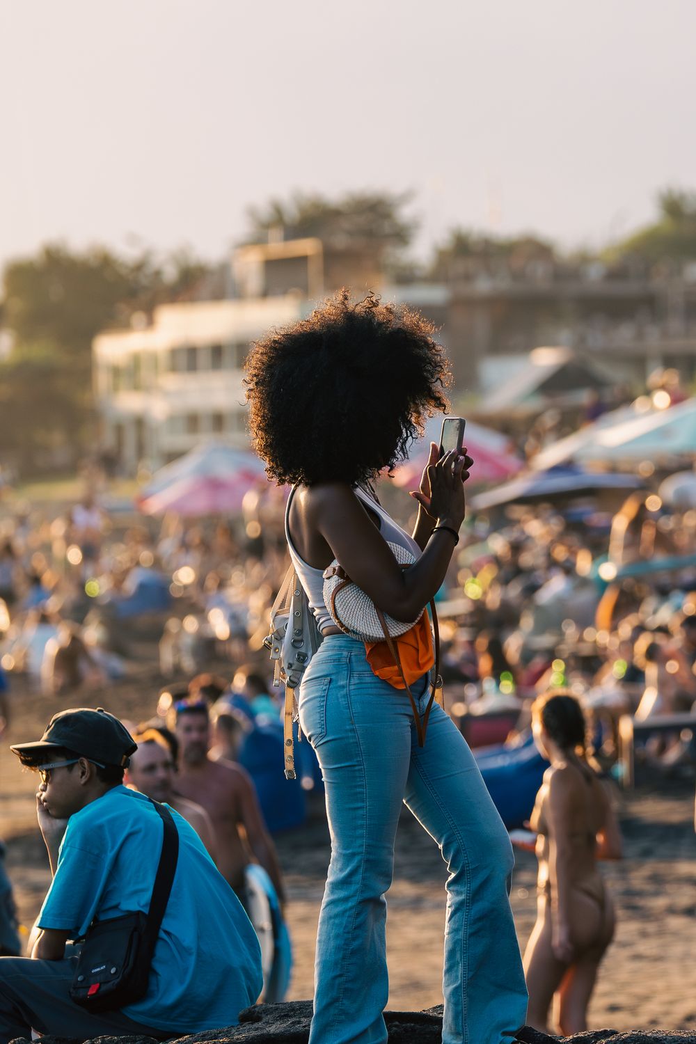 A sequence of photos showing a person with curly hair taking pictures at a crowded beach during sunset.