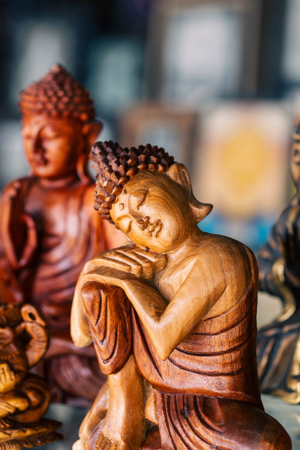 Wooden carved Buddha statues in varying shades of brown displayed in a row showing different meditative poses.