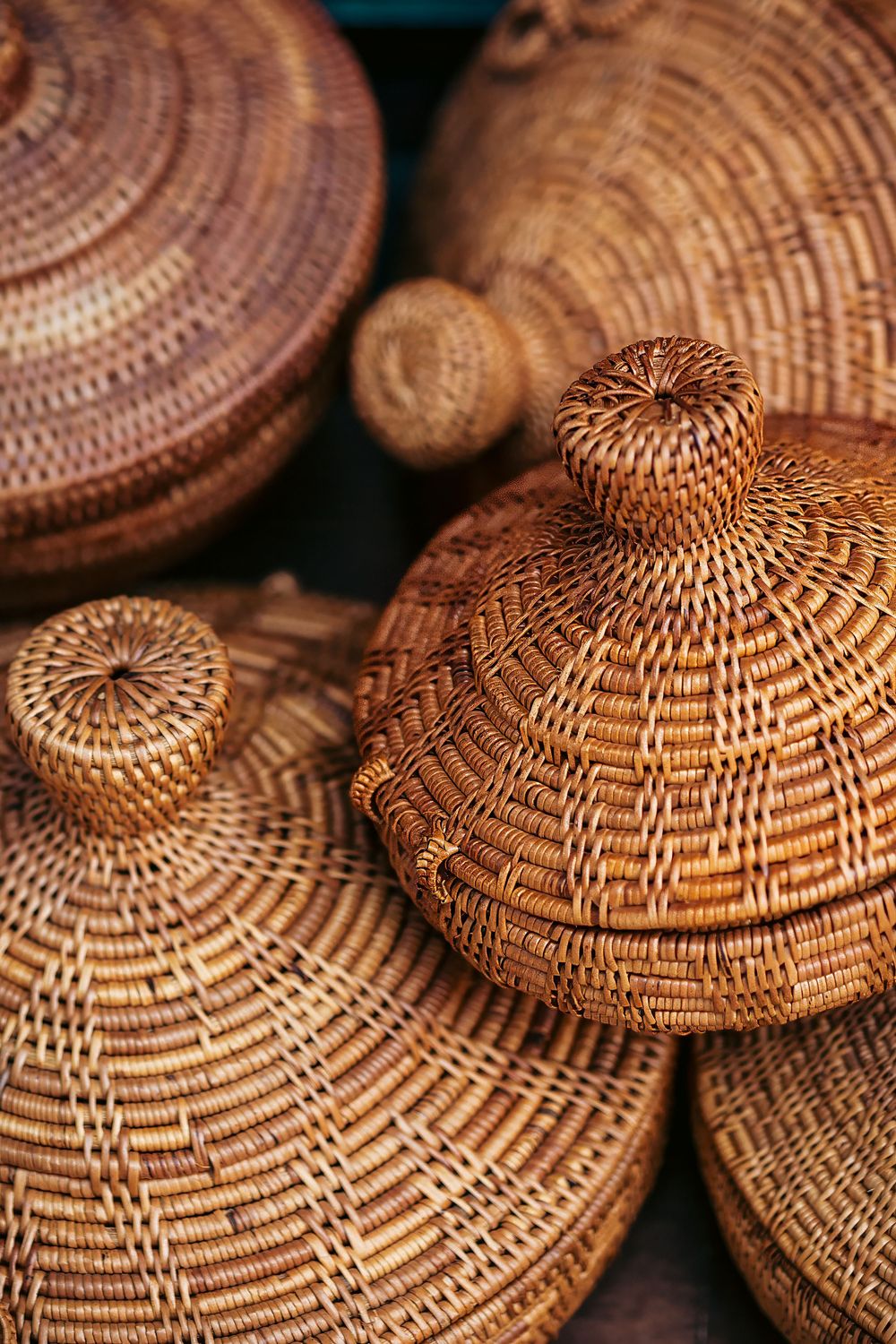 Close-up of handwoven rattan or wicker baskets with domed lids showing intricate spiral weaving patterns in warm brown tones.