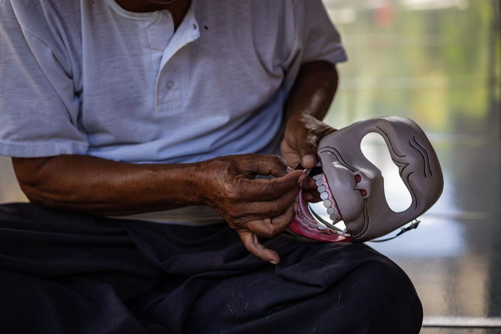 Hands holding a white and black decorative mask in contemplative pose.