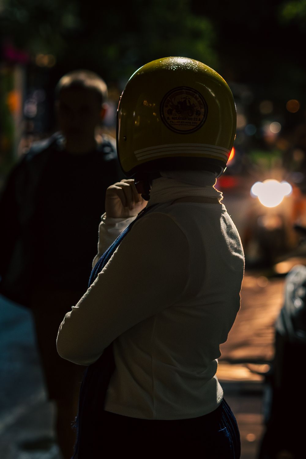 A person wearing a yellow motorcycle helmet stands in a dimly lit street at night.
