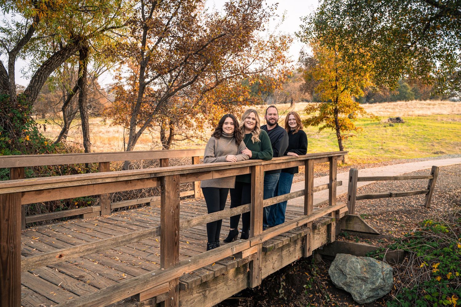Family group poses together on wooden bridge during autumn afternoon.
