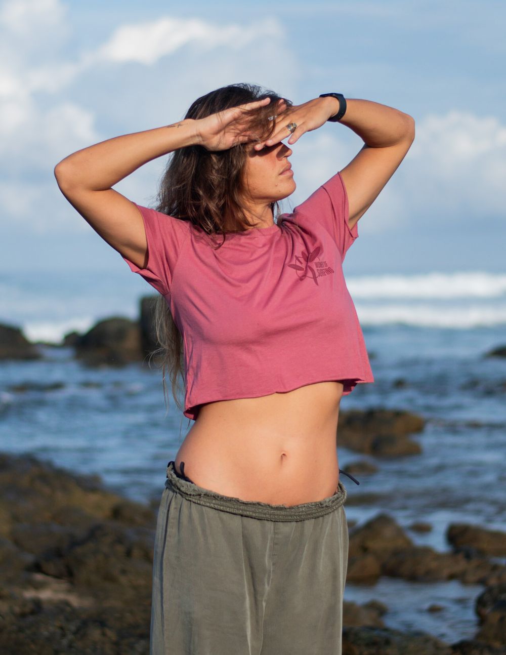 A person stretches on a rocky beach with ocean waves in the background.
