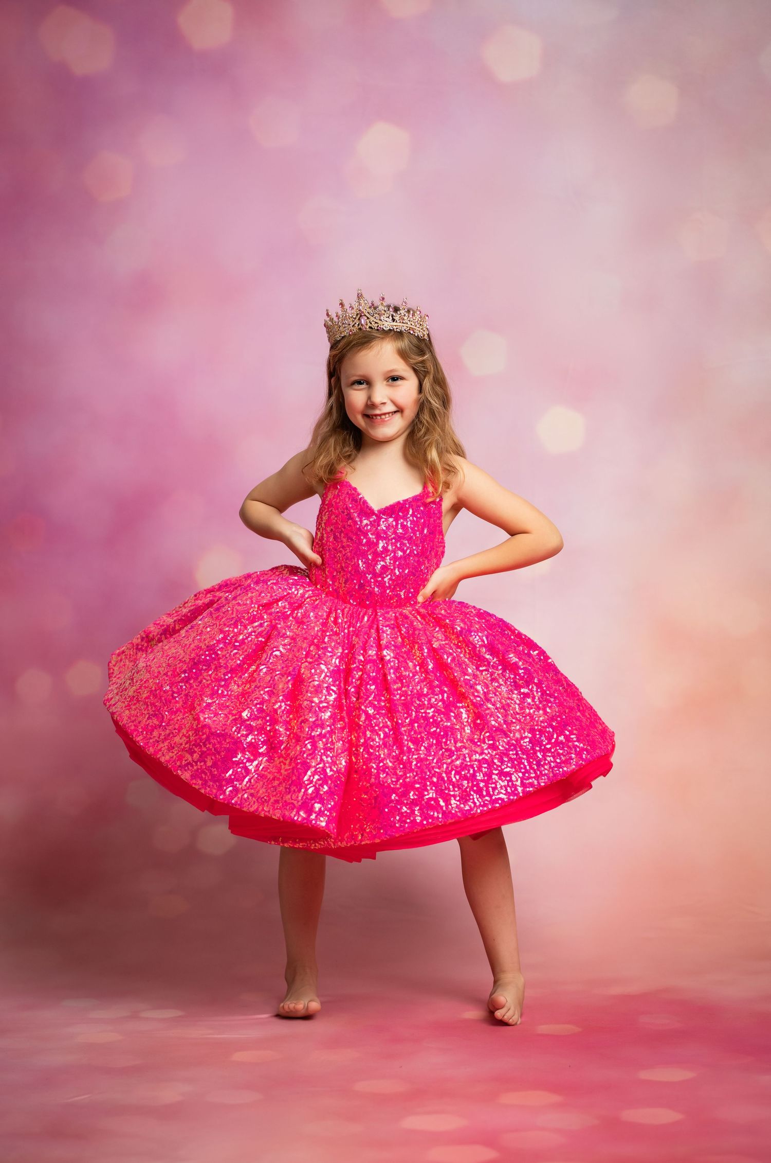 A sparkly hot pink princess dress twirls on a pink bokeh background, complete with a delicate crown and bare feet.