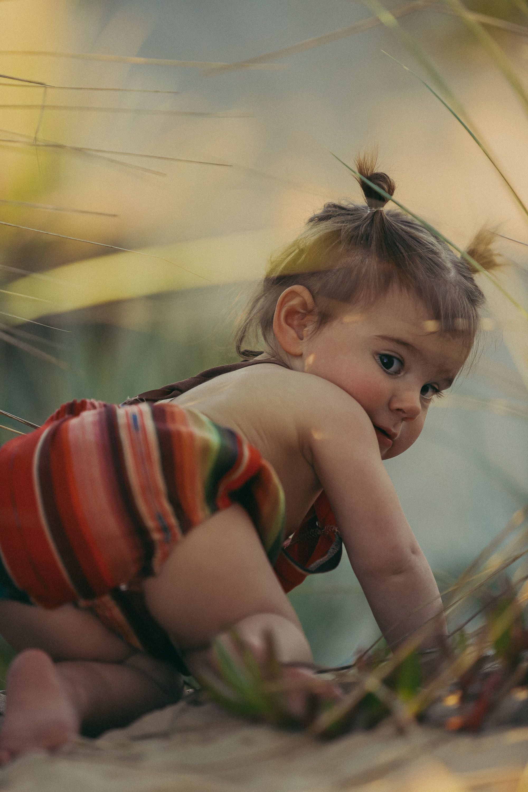 Small child in striped romper crawling and exploring on the ground.