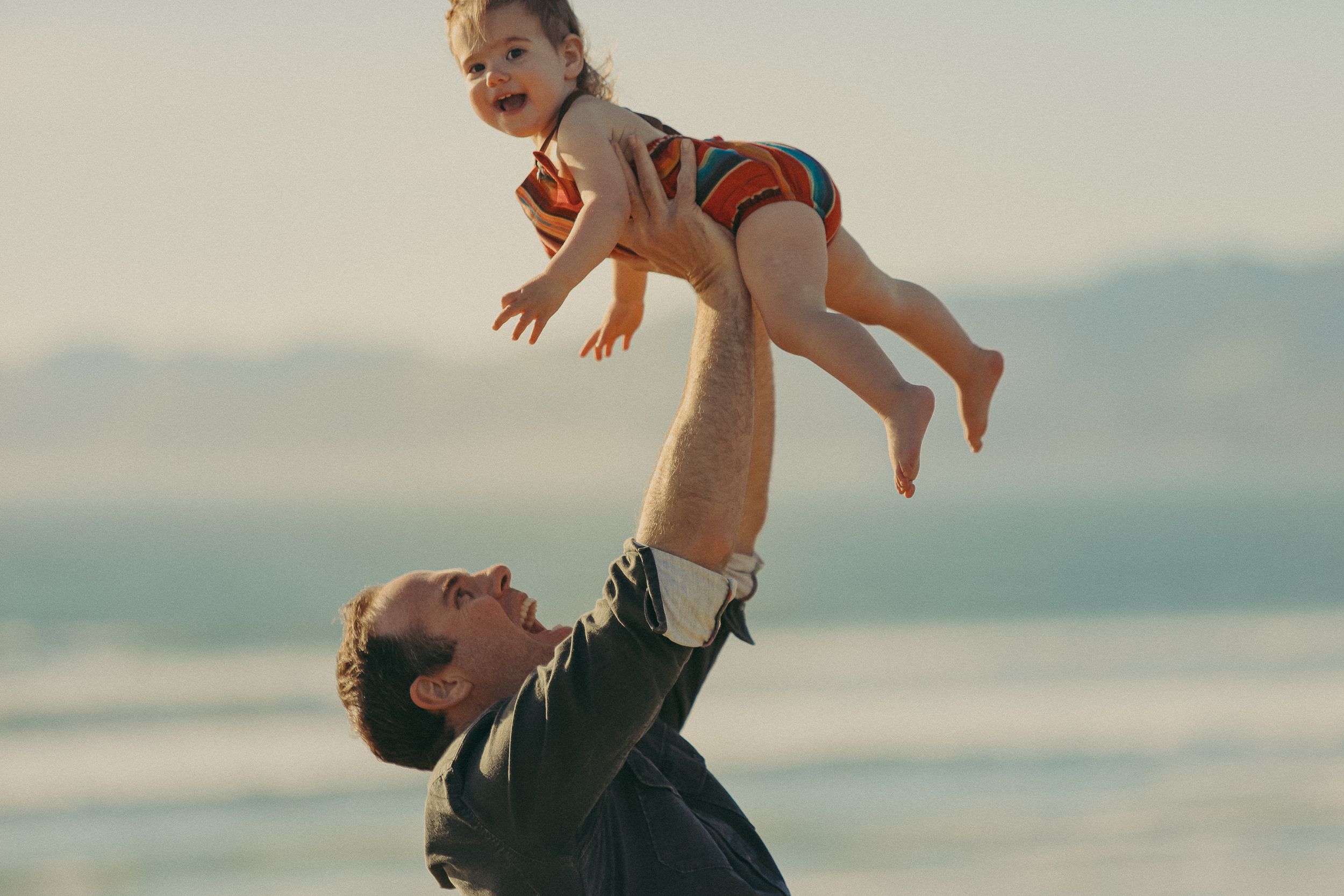 Joyful moment captured as a child is lifted high in the air at the beach.
