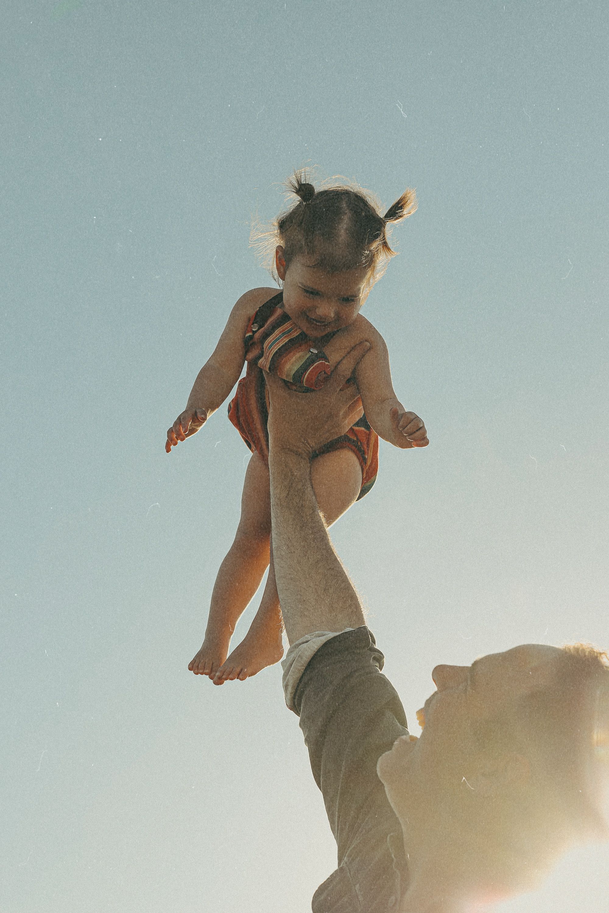 Silhouette of child being lifted high into the air during sunset.