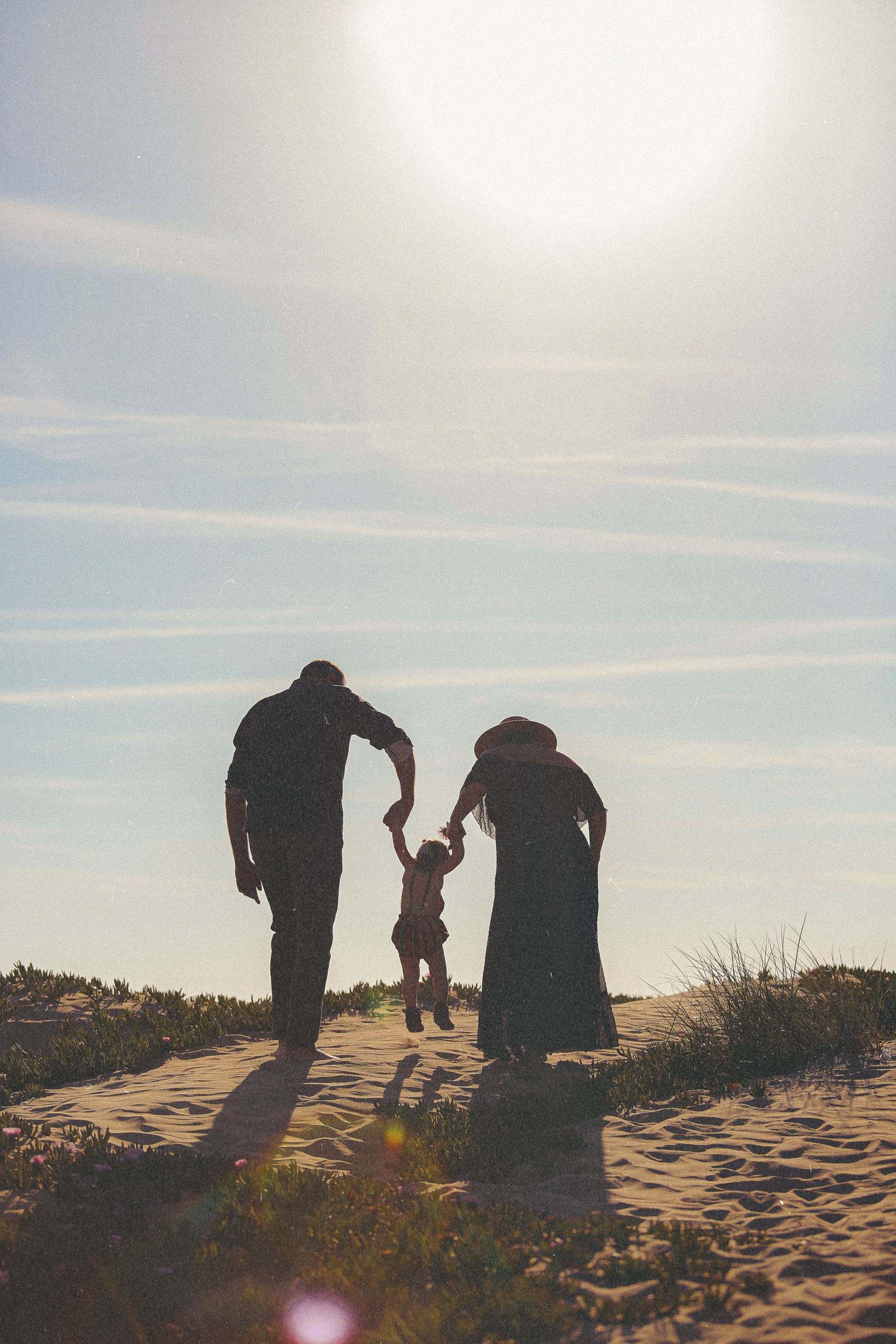 Silhouetted family holding hands and walking together on sandy dunes at sunset.