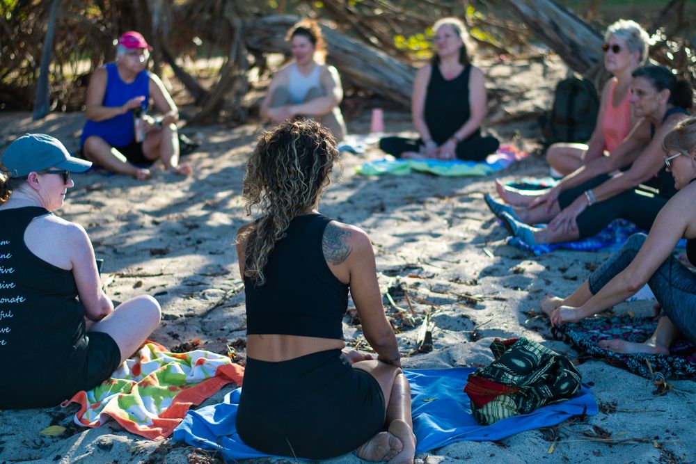 Beach yoga class participants sitting in circle on sand during outdoor session.