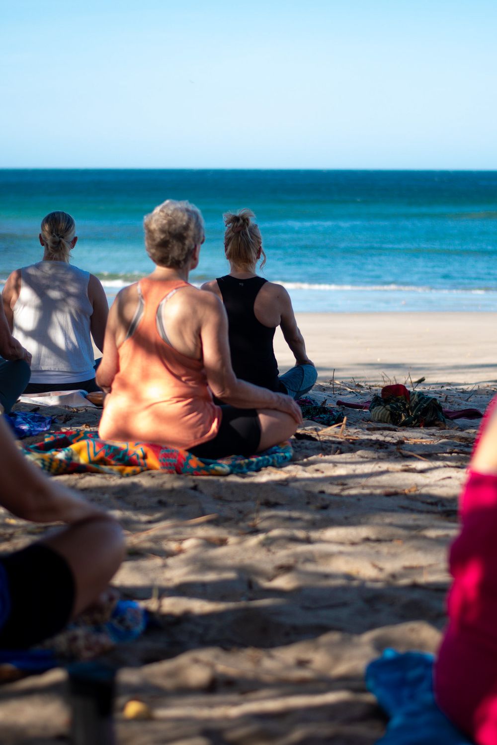 Group relaxing on beach blankets looking out at turquoise ocean waters.