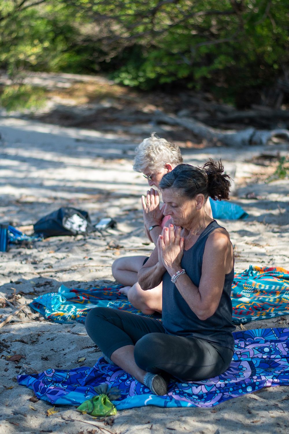 People practicing outdoor meditation on colorful blankets in a natural setting.