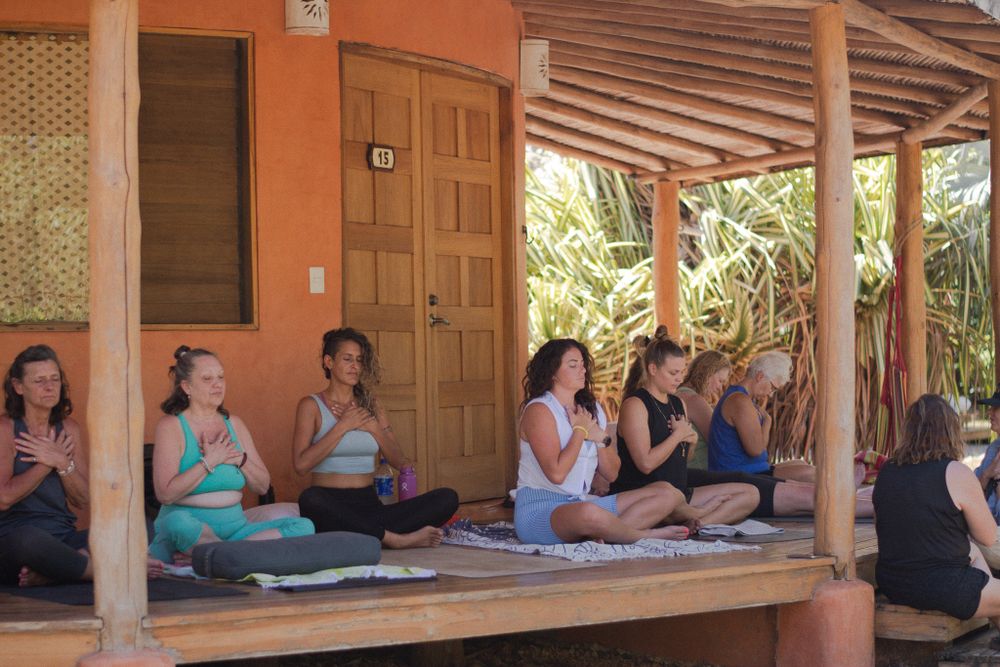 Group meditation session on a covered porch with orange walls.