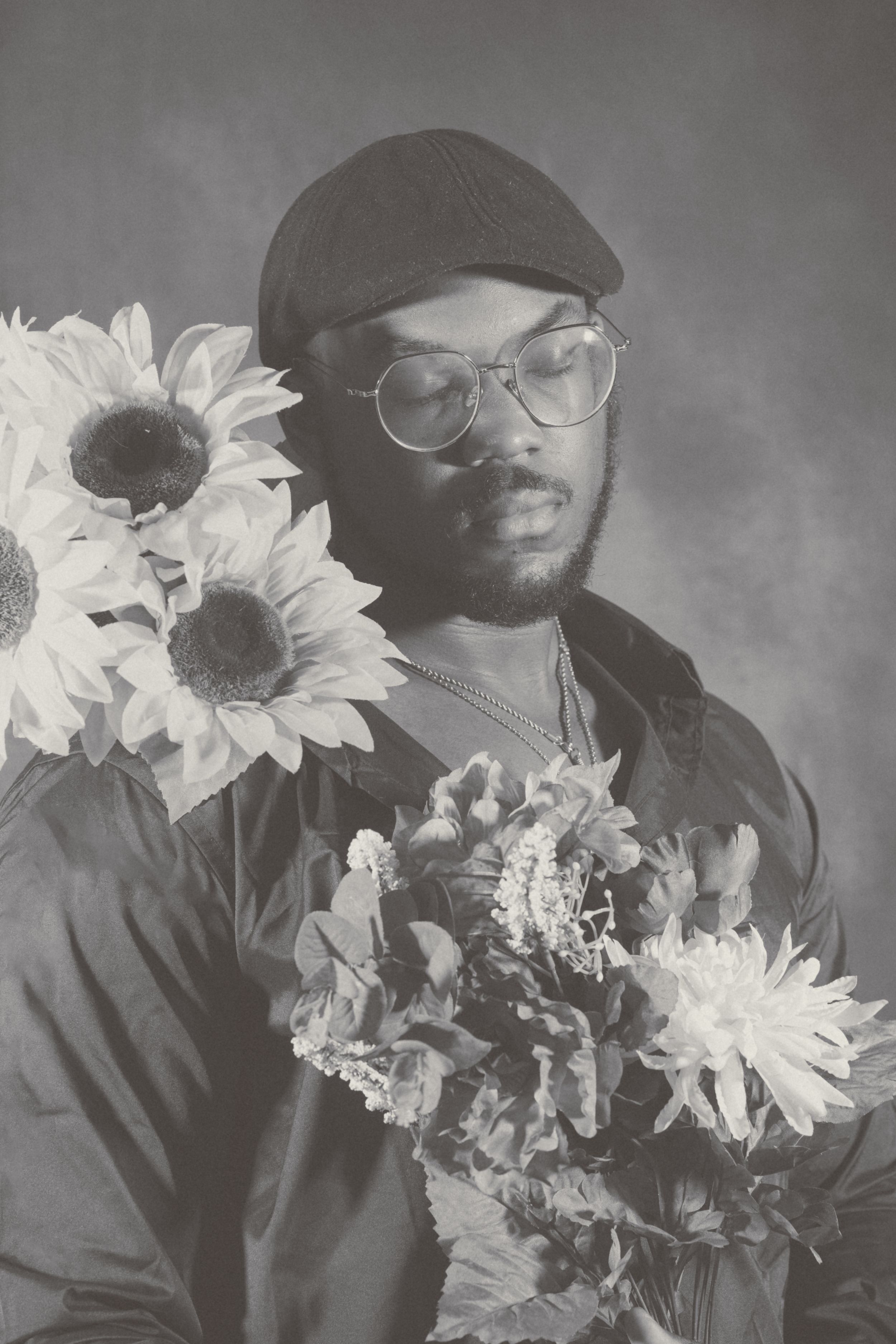 Artistic black and white photograph of sunflowers arranged in front of someone wearing dark clothing.