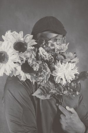 Dramatic black and white portrait showing someone holding flowers near their face while wearing dark clothing.
