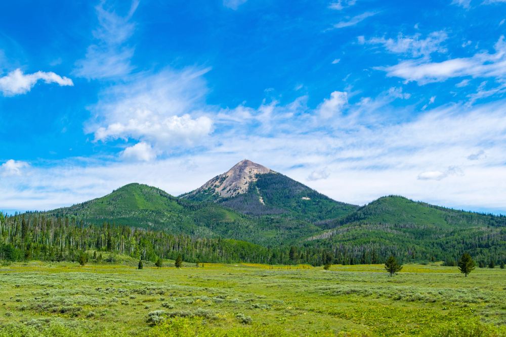 Majestic mountain peak rises above green meadow under bright blue summer sky.