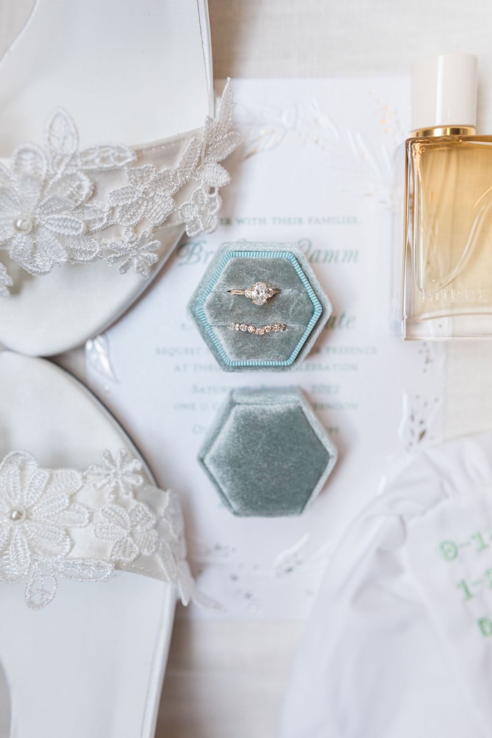 Wedding accessories including rings, perfume bottle and lace details arranged on white surface.