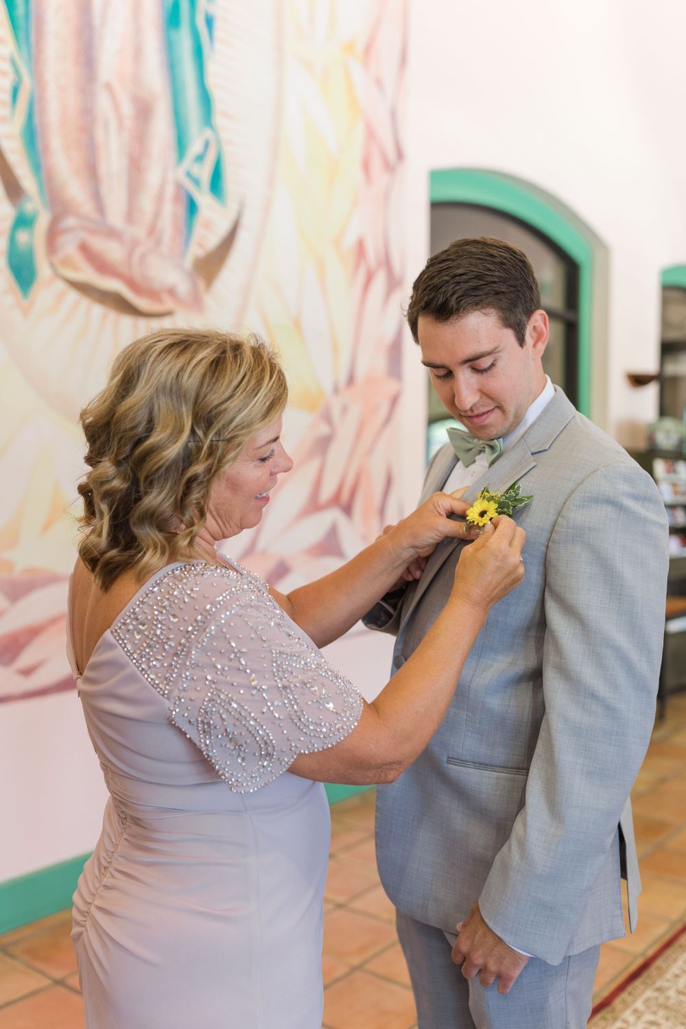 Mother helps pin boutonniere on groom's lapel before wedding ceremony.