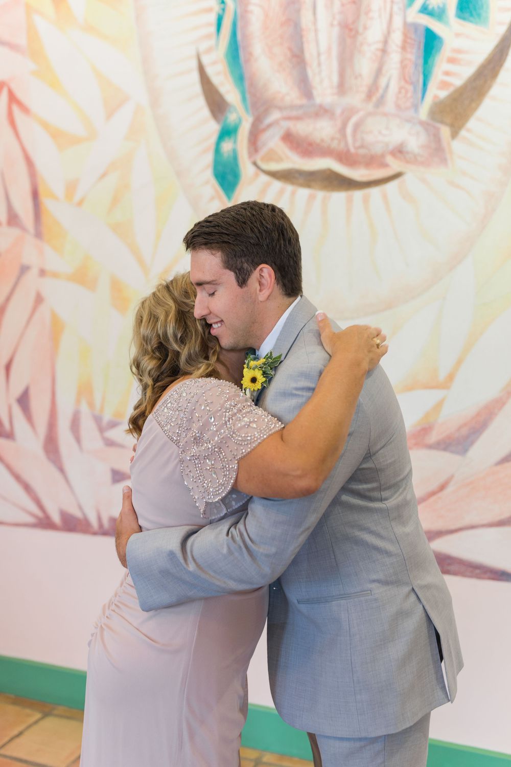 Couple sharing an intimate embrace during first look moment against soft pastel backdrop.