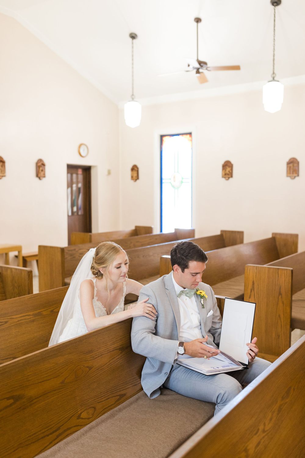 Newlyweds sitting together in wooden church pew reviewing ceremony details.